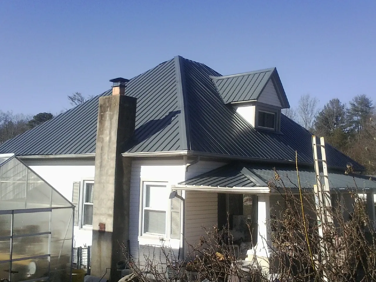 Dark blue standing seam metal roof on a white farmhouse with dormer — Slate & Tile Roof Repair by Roofing Brothers in Hennepin