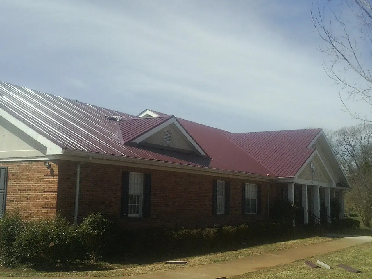 Red metal roof with gabled entries on a long brick building, from a Hail Damage Roof Repair job in Hennepin