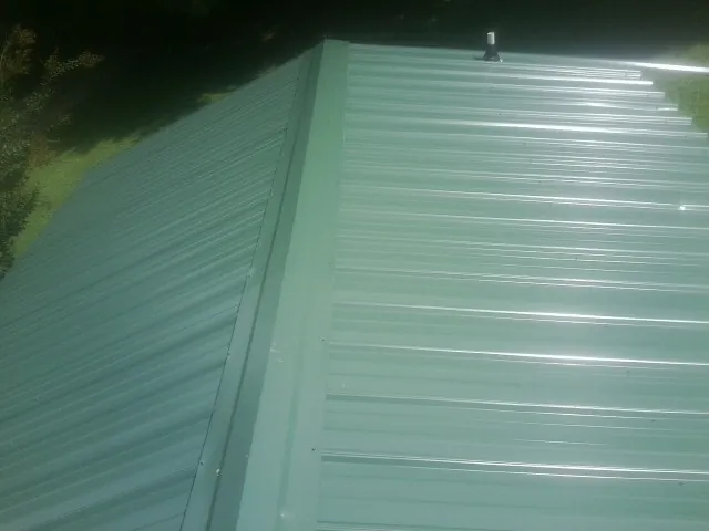 New green metal panels meeting at the ridge of a roof — Flat Roof Repair work by our crew in Hennepin