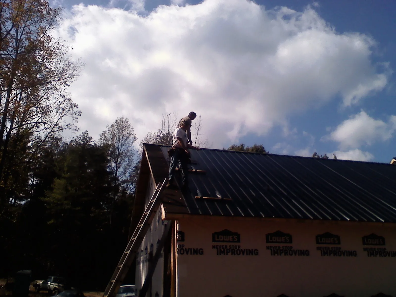Roofer fastening dark metal panels high against a cloudy sky, from a Roof Inspection job in Hennepin