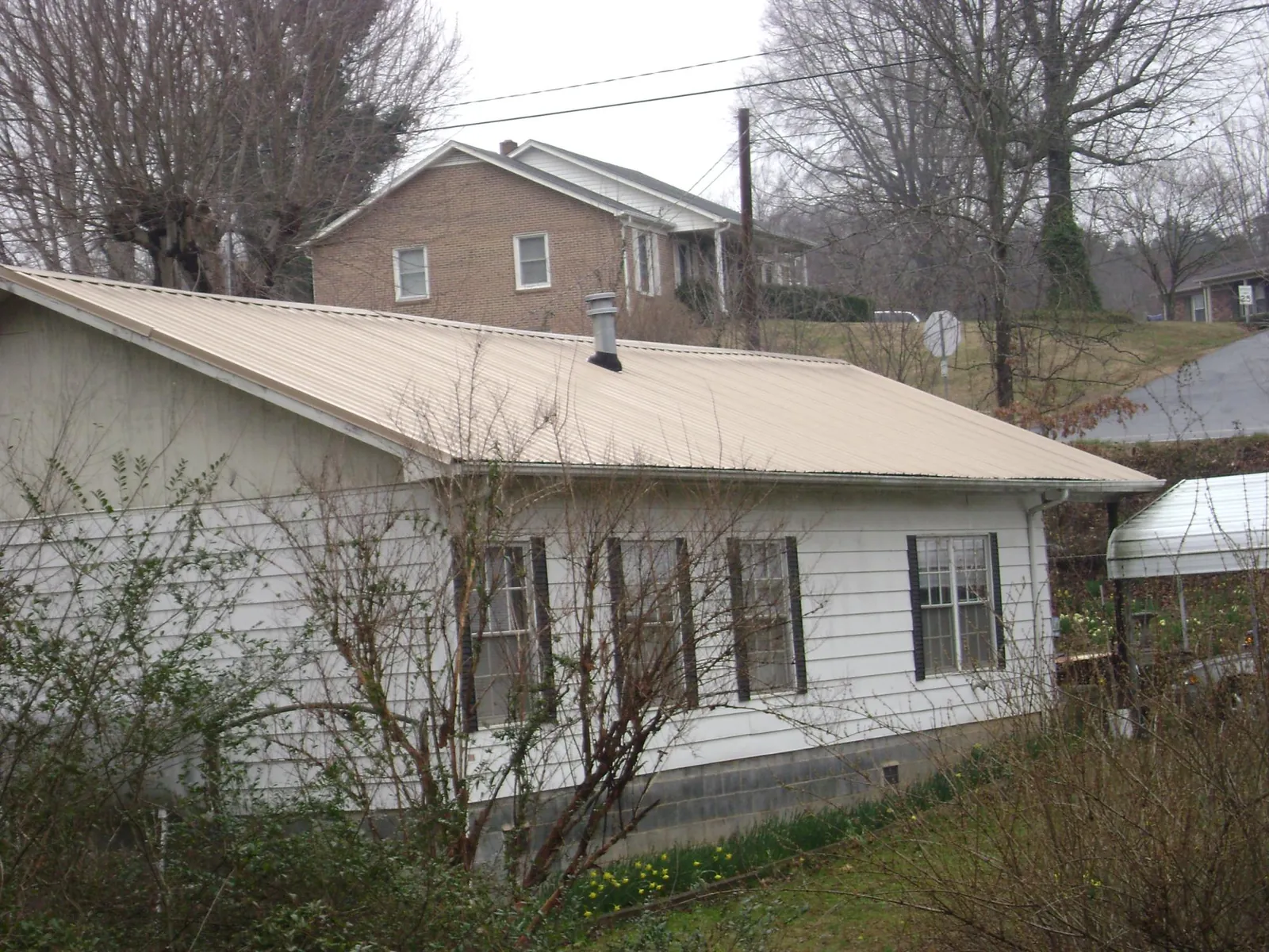 Tan metal roof on a white sided house set into a hillside — Commercial Roofing by Roofing Brothers in Hennepin