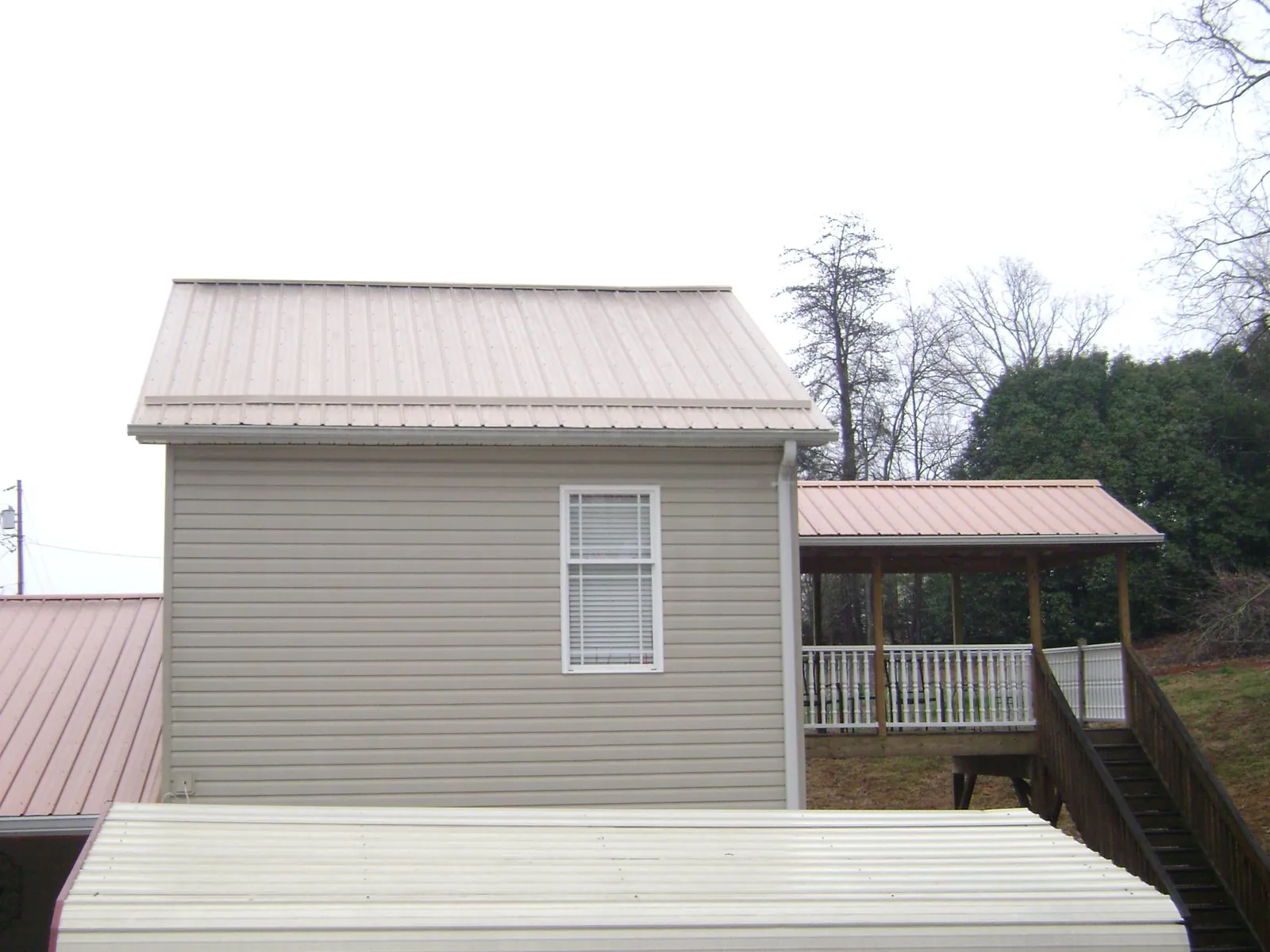 Tan metal roofs on a two story addition and attached porch, from a Roof Replacement job in Hennepin